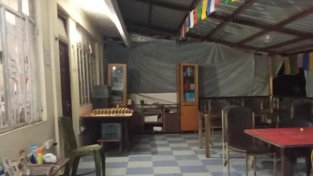 A room with a checkered floor, tables, chairs, and a ceiling with colorful flags. - Backpackers Hostel  (Darjeeling)