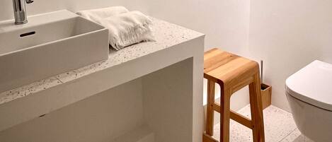 A bathroom with a white sink, wooden stool, and a toilet.