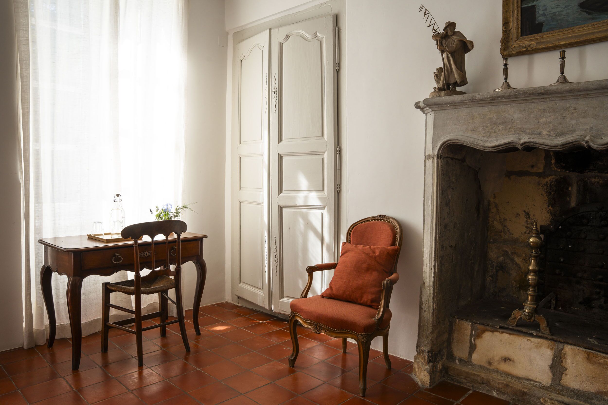 A room with a wooden desk, a chair, a white door, and a fireplace.