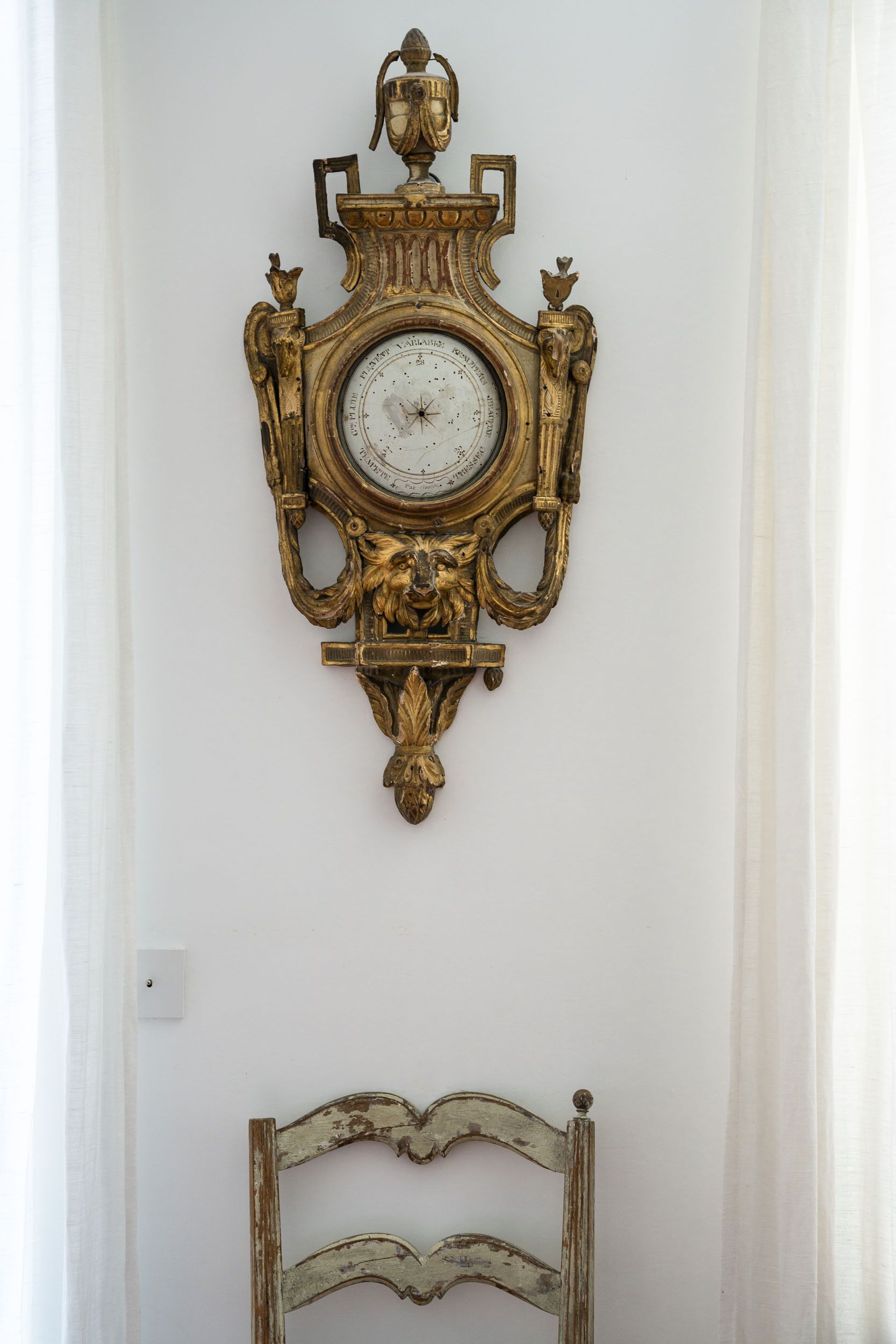 A wall-mounted ornate clock with a lion motif, a rustic wooden bed frame, and a white wall.