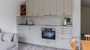 Una cocina compacta con horno integrado, cafetera y un pequeño comedor con mesa y silla de madera.