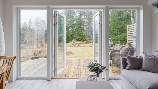 Una habitación con puerta corrediza de vidrio que da a una terraza exterior, un sofá gris y una silla de madera.