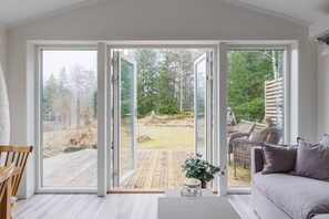 Une pièce dotée d’une porte-fenêtre coulissante donnant sur une terrasse, d’un canapé gris et d’une chaise en bois.