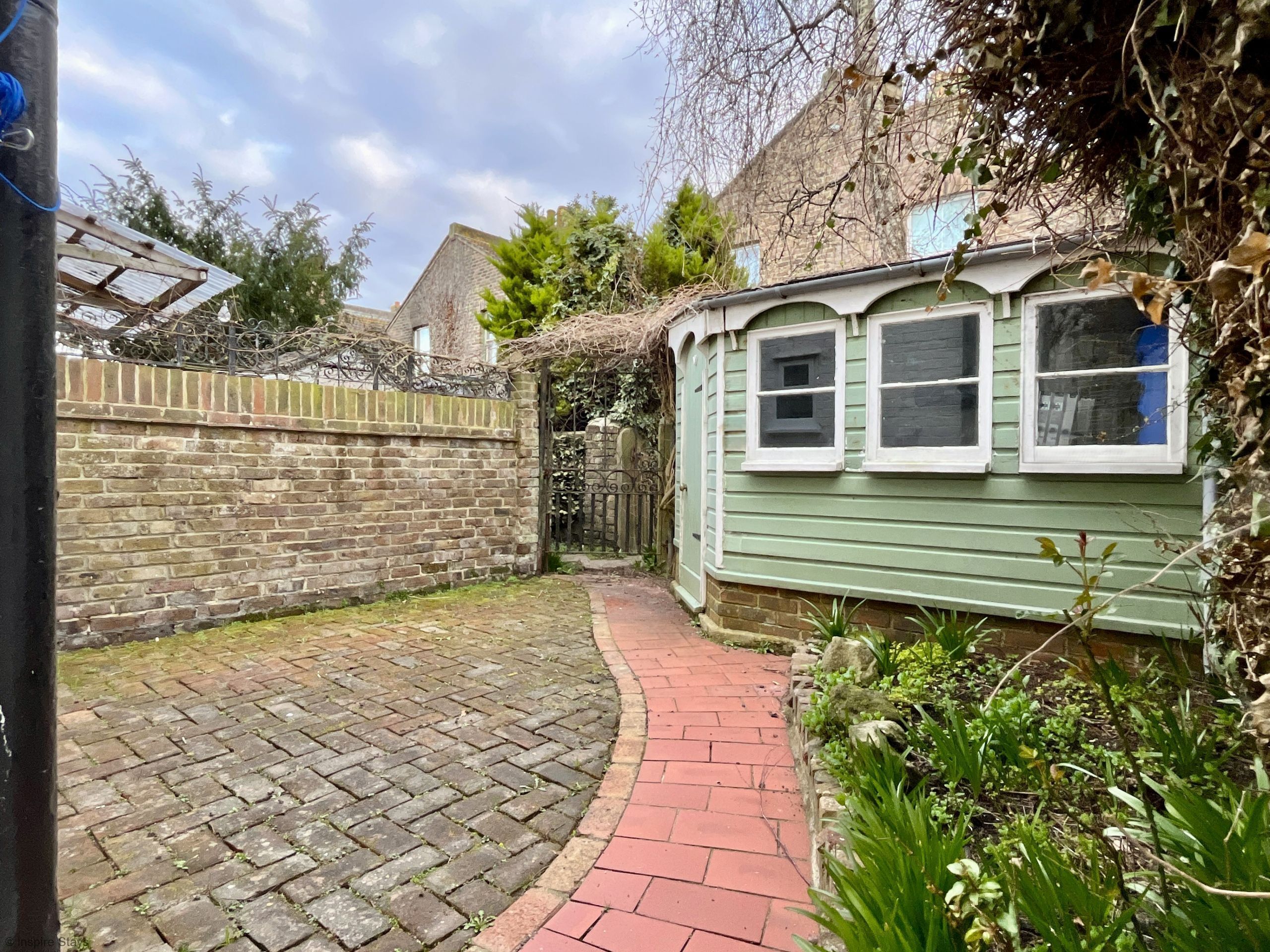 A narrow brick pathway leading to a green building with a window.