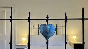 A bed with a metal frame and a heart-shaped decoration, two bedside tables with lamps, and neatly folded towels.