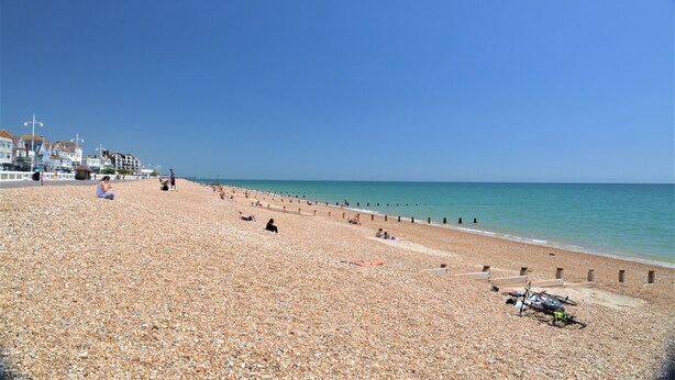 A pebbled beach with people sunbathing and a bicycle parked near the water.