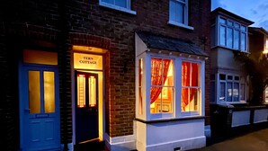 A brick cottage with a blue door and a small window with red curtains.