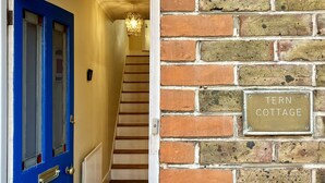 A blue door with a window, a staircase, and a brick wall with a sign reading "TERN COTTAGE".