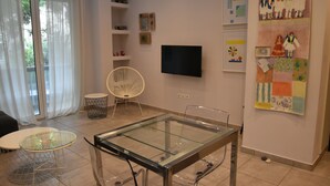 Ein modernes Wohnzimmer mit einem Esstisch mit Glasplatte, einem weißen Stuhl und einem an der Wand montierten Flachbildfernseher.