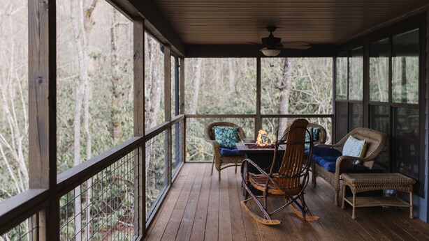 A covered porch with wooden flooring, wicker furniture, and a ceiling fan.