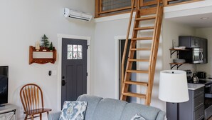A loft-style living space with a wooden ladder, a sofa, a TV, and a kitchen area.