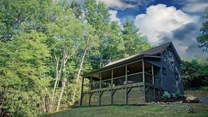 A cabin with a porch, surrounded by dense trees.