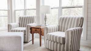 A room with striped armchairs, a small wooden table with a lamp, and a matching ottoman.