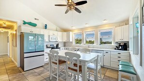 A modern kitchen with white cabinetry, a central island with seating, a ceiling fan, and a view through large windows. - Relaxing family and dog friendly getaway located in Hatteras (Hatteras)