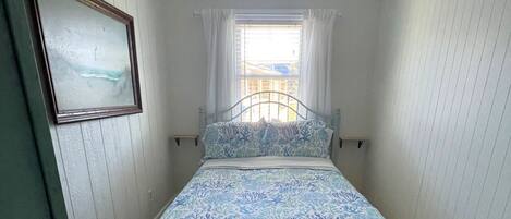 Un dormitorio con cama, ventilador de techo, ventana con cortinas e imagen enmarcada en la pared.