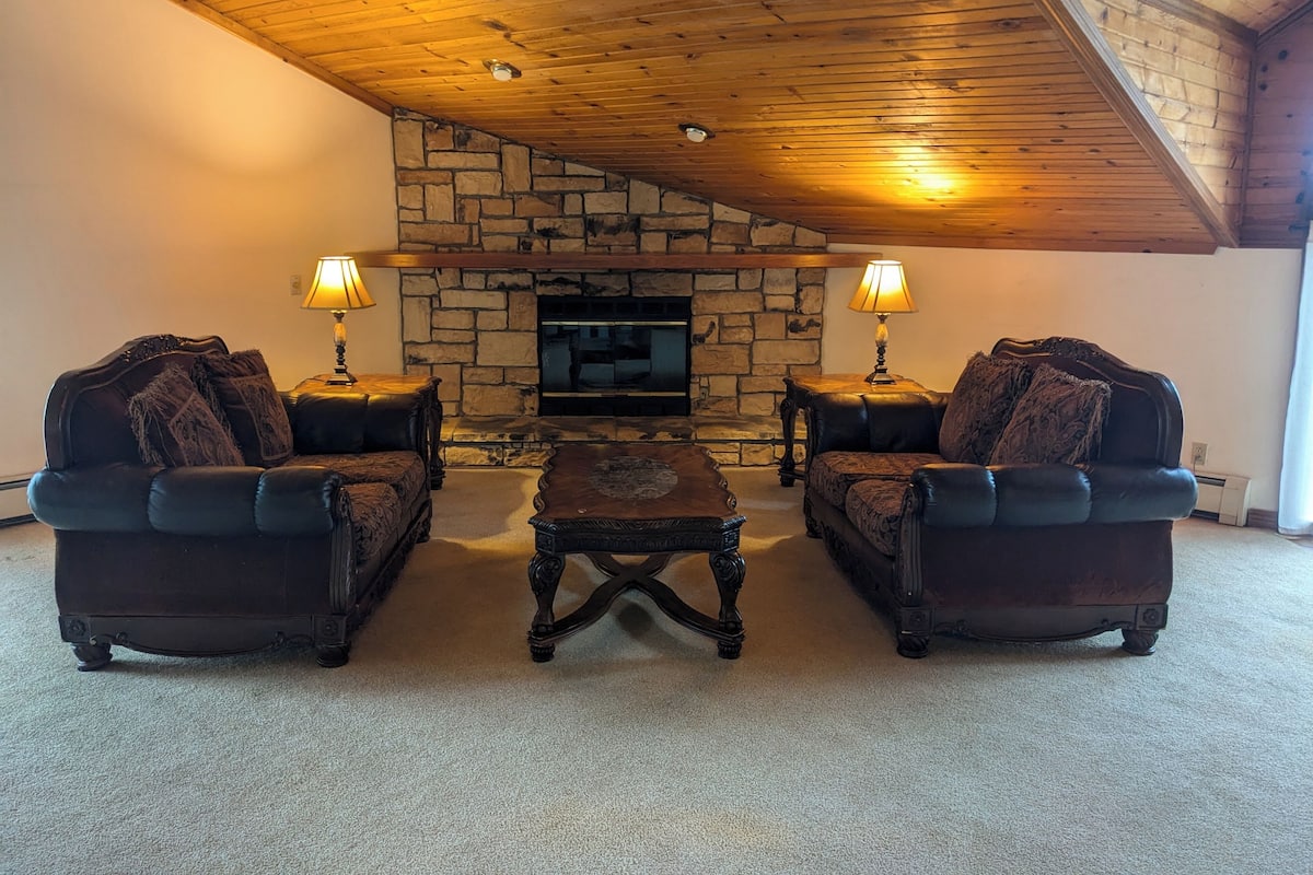 A cozy living room with a stone fireplace, two leather armchairs, and a matching coffee table.