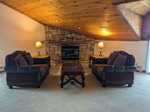 A cozy living room with a stone fireplace, two leather armchairs, and a matching coffee table. - The Carriage House Inn Bed and Breakfast (Meadville)