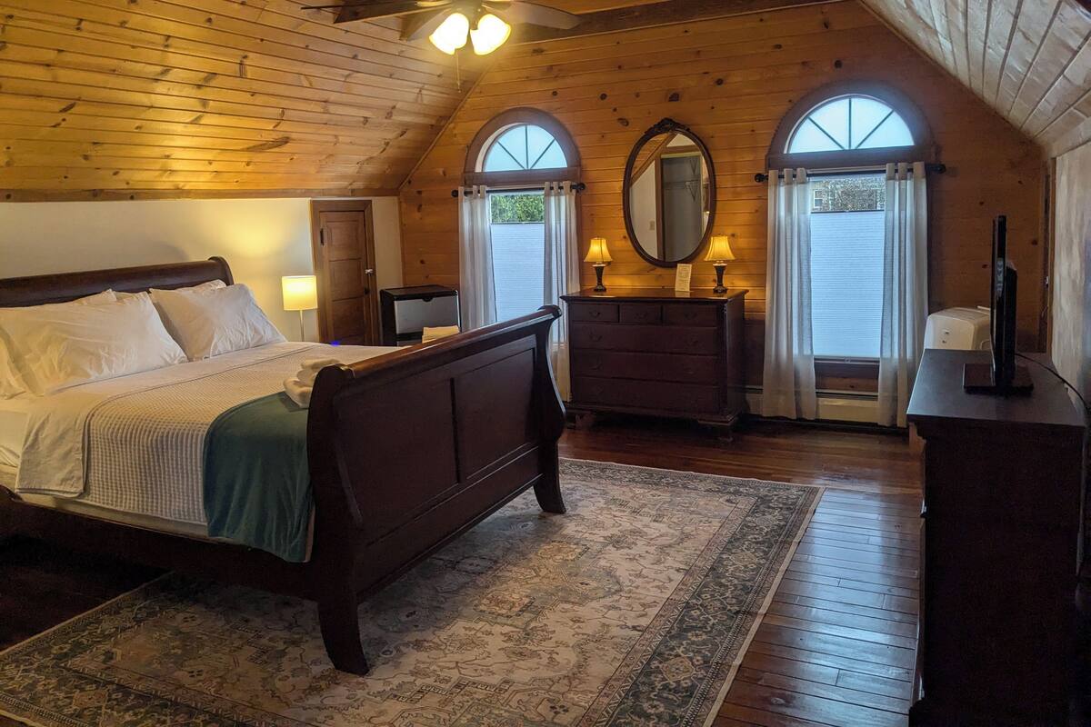 A bedroom with a wooden ceiling, a bed, a dresser, a mirror, and a television.