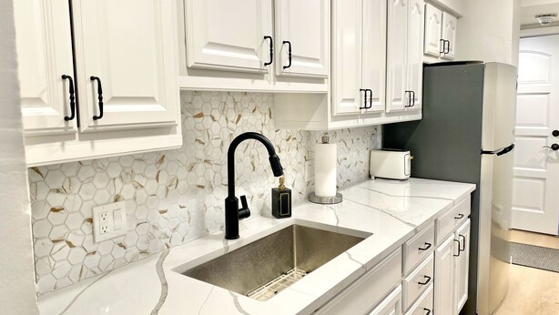 Eine Küche mit weißen Schränken, einer Marmor-Spritzschutzleiste, einem schwarzen Wasserhahn, einem Toaster und einem Kühlschrank.