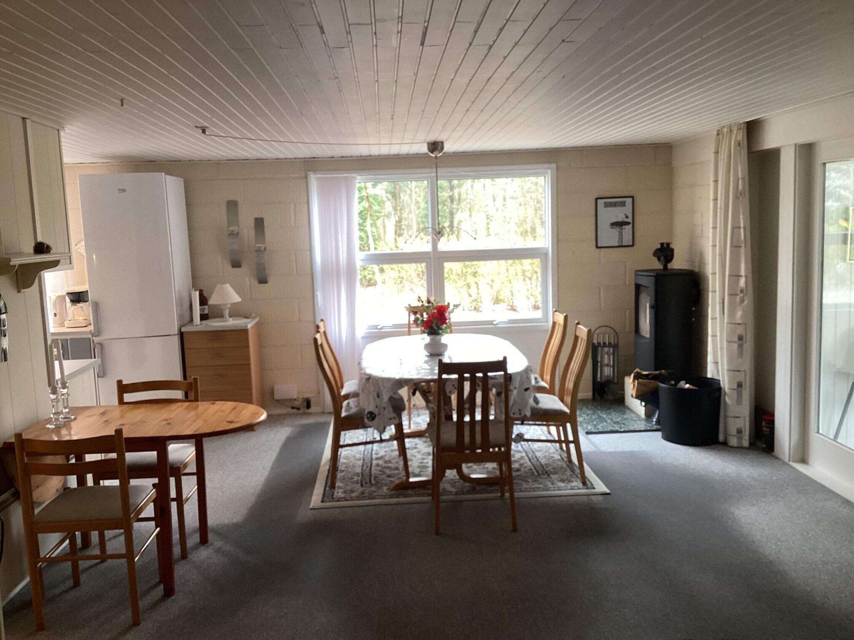 A dining area with a round table and chairs, a refrigerator, a window with curtains, and a fireplace.