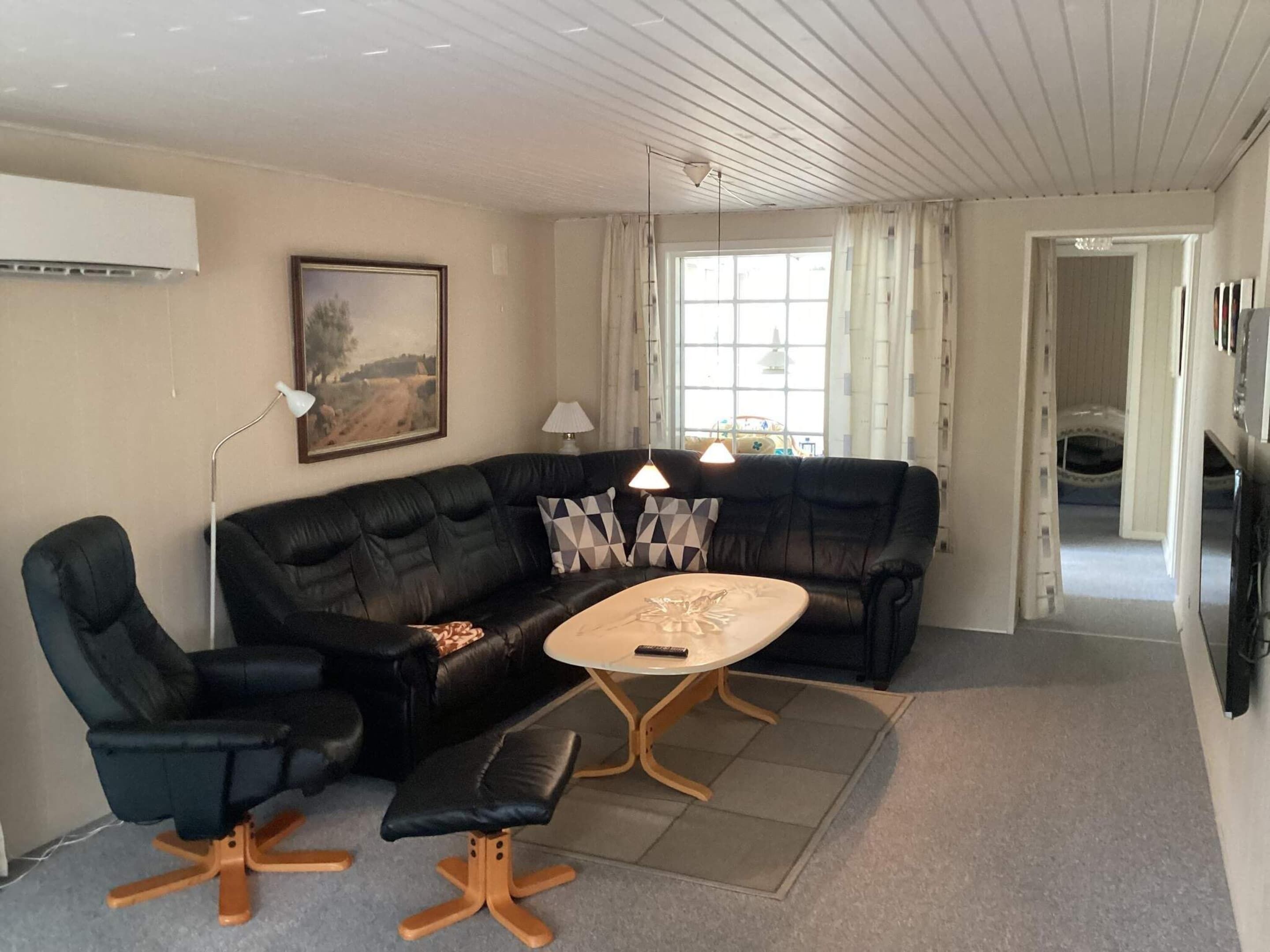 A living room with a black leather sofa, a small round table, a black office chair, a lamp, and a painting on the wall.
