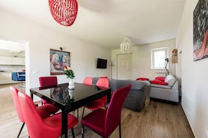 A modern living space with a dining area, a gray sofa, and a red chair. - The Little Villa With Garden(4 rooms, Free Parking) (Lucca)