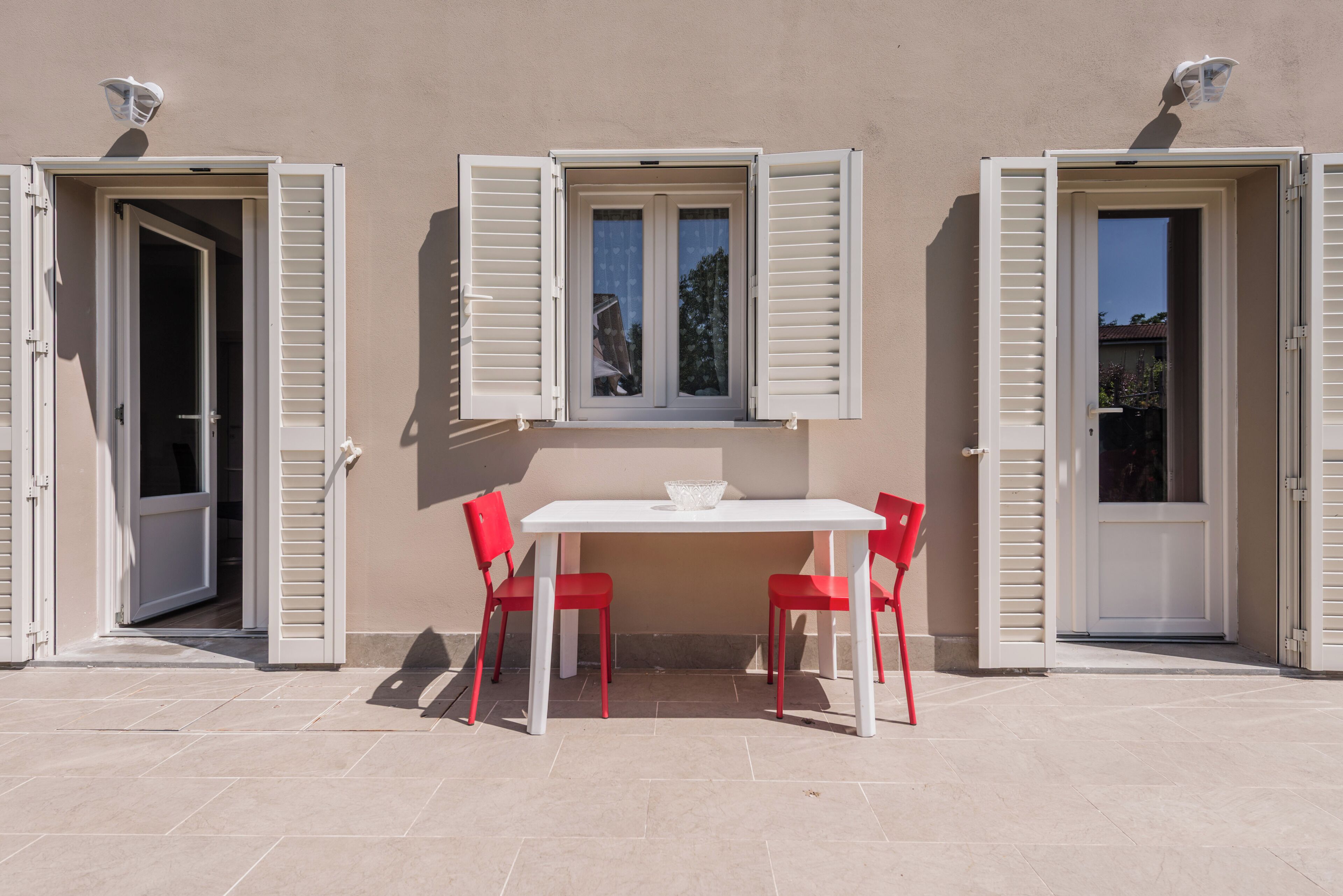 An outdoor seating area with a table and chairs, a window with shutters, and a door.