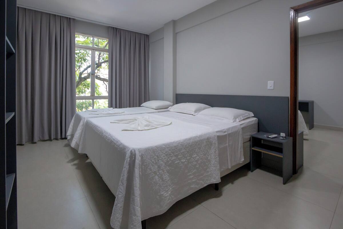 A hotel room with a large bed, a bedside table, a mirror, and a window with curtains.