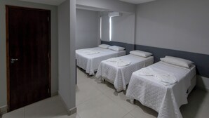 Egy szállodai szoba, amelyben három egyágyas ágy, egy fa ajtó és fehér csempézett padló található.