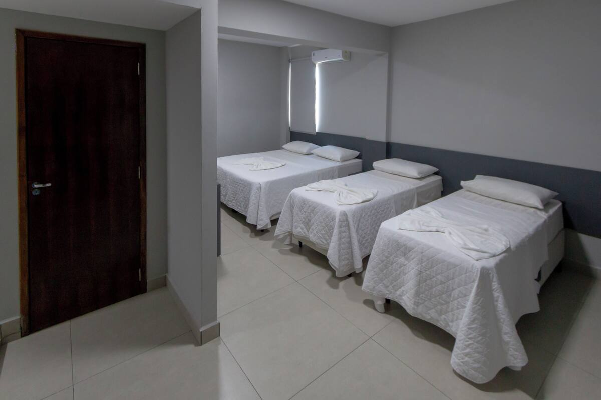 A hotel room with three single beds, a wooden door, and a white tiled floor.