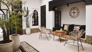 Un intérieur chaleureux avec un canapé noir, des fauteuils en osier, une table basse en bois et des plantes en pot.