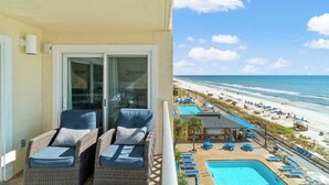 A balcony with wicker chairs and a glass door leading to a pool area with lounge chairs and umbrellas.
