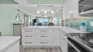 A kitchen with white cabinets, a large island, and a backsplash with a 'BEACH' sign.
