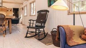 A cozy room with a wooden rocking chair, a dining table with chairs, and a large window with a view of trees. - 4 Star Holiday Home in Liseleje (Liseleje)