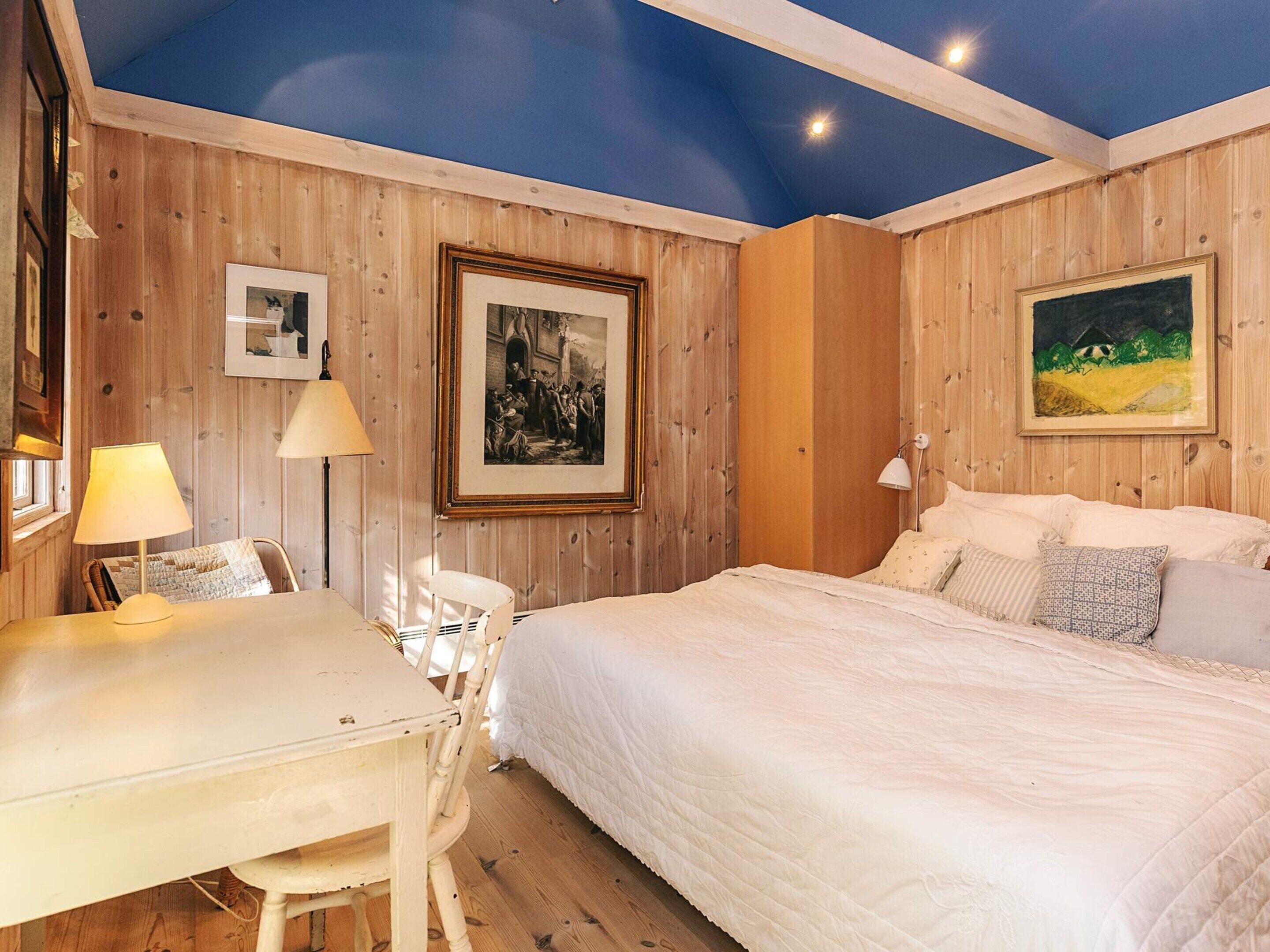 A room with a bed, a desk, and chairs. There are framed pictures on the walls.