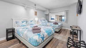 A modern bedroom with two beds, a TV, and a view of the sea.
