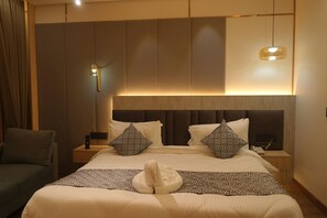 A hotel room with a large bed, two nightstands, a sofa, and a hanging light fixture.