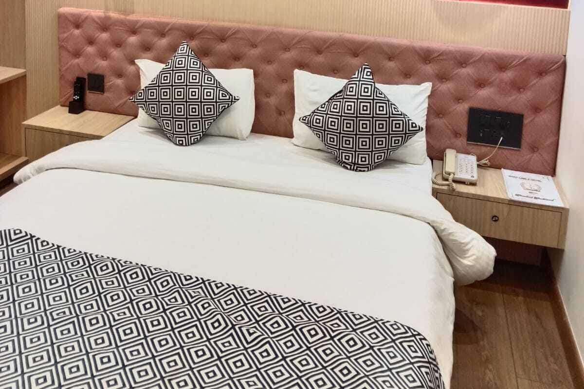 A hotel room with a tufted headboard, a bed with patterned bedding, bedside tables with lamps, and a red accent wall.