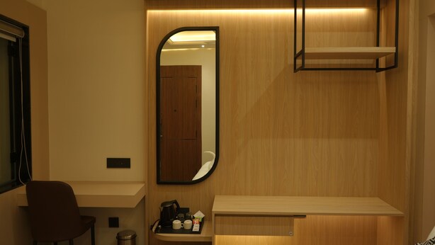 Ein modernes Hotelzimmer mit einer Holzvertäfelung, einem großen Spiegel, einem Schreibtisch mit Stuhl, einer kleinen Ablage mit Toilettenartikeln und einem Hängebrett.