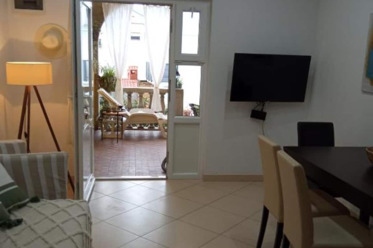 A room with a dining table, chairs, a TV mounted on the wall, and a view of the outside balcony area.