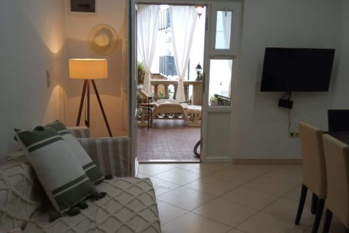 A room with a bed, a desk, a chair, a TV, a lamp, and a view of an outdoor balcony.