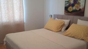 Ein ordentlich bezogenes Bett mit weißer und beiger Bettdecke, zwei gelbe Kissen und einem Kopfteil mit floralem Gemälde.
