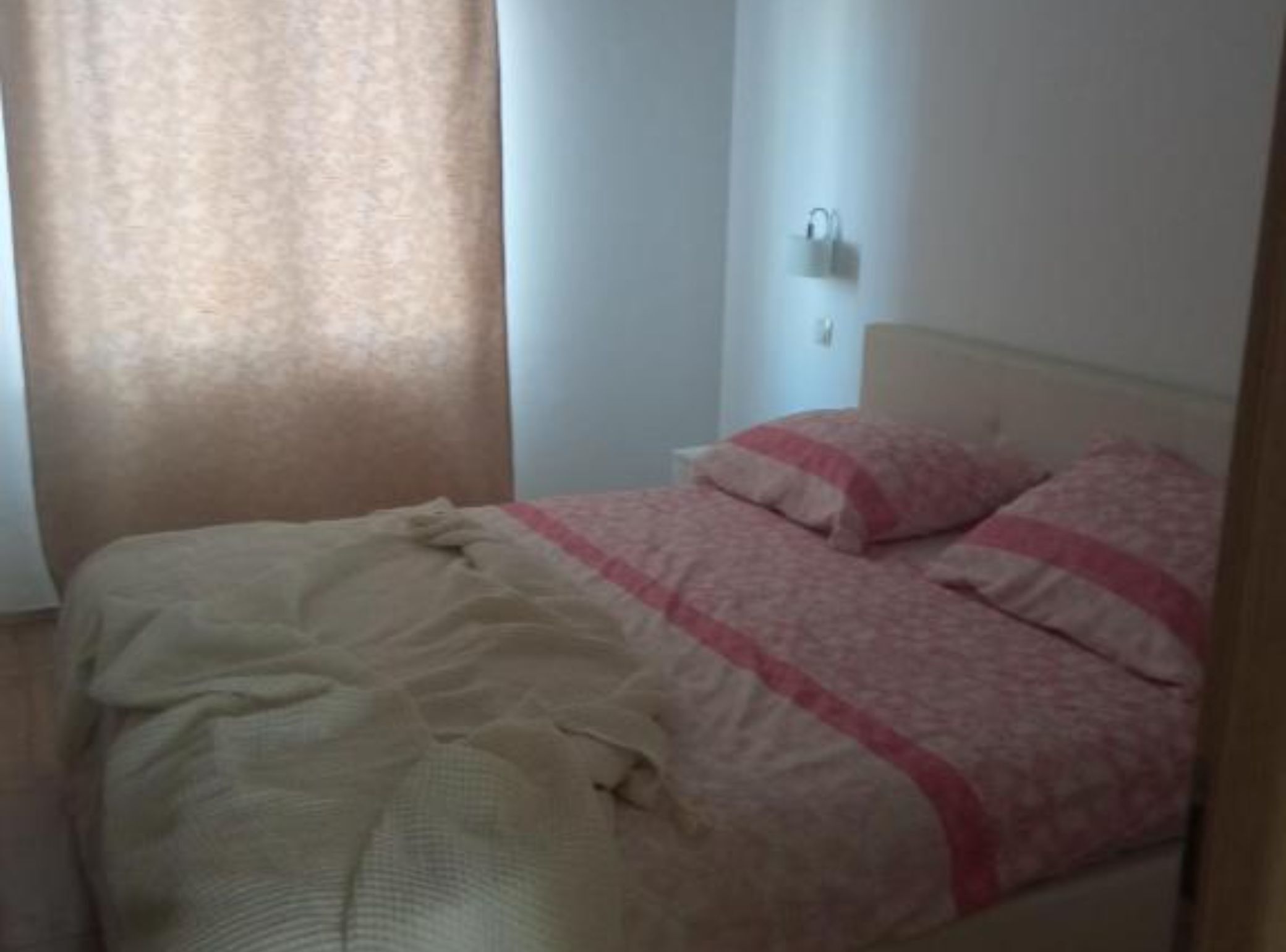 Una camera da letto con un letto, un comodino, una lampada a parete e una finestra con tende.