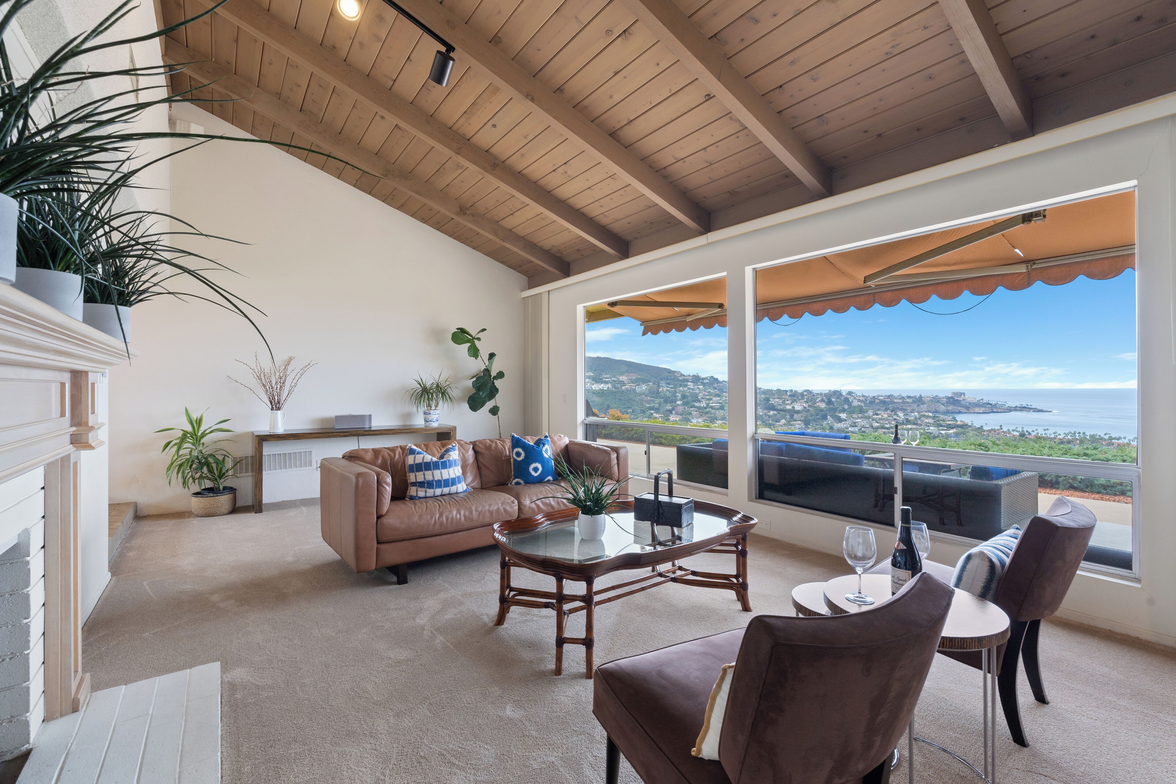 Un'ampia zona giorno con soffitto in legno, una grande finestra con vista sul mare, un divano in pelle marrone, un tavolino da caffè in vetro e un tavolo da pranzo con sedie.
