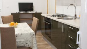 A compact kitchen with a dining area, including a table with a fruit bowl, a TV, and a stove. - Apartments Ruzarija (Marina)