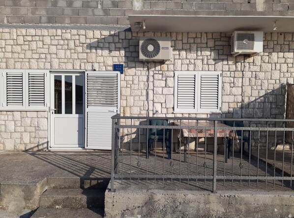A stone building with a white door, two windows with shutters, and an air conditioning unit on the wall.