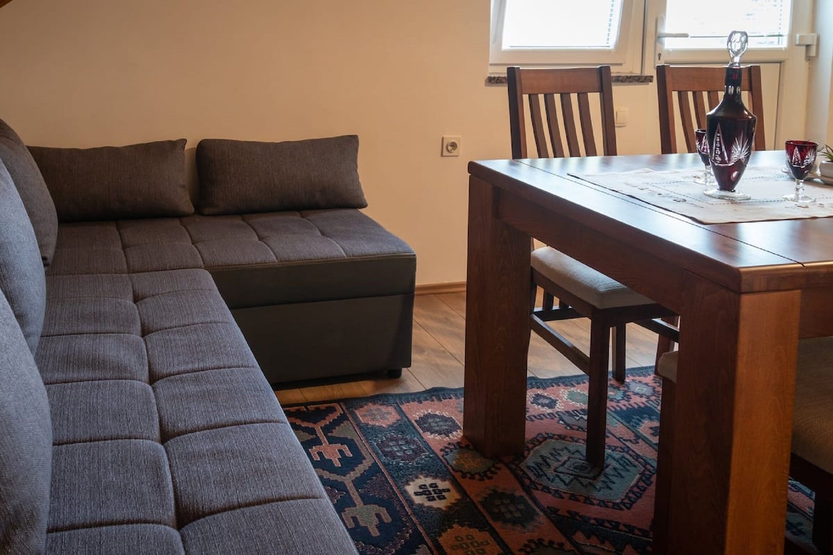 Um espaço de estar moderno com sofá seccional, mesa de jantar de madeira e tapete estampado.
