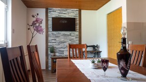 A dining area with a wooden table, chairs, a television mounted on a stone wall, and a sewing machine.