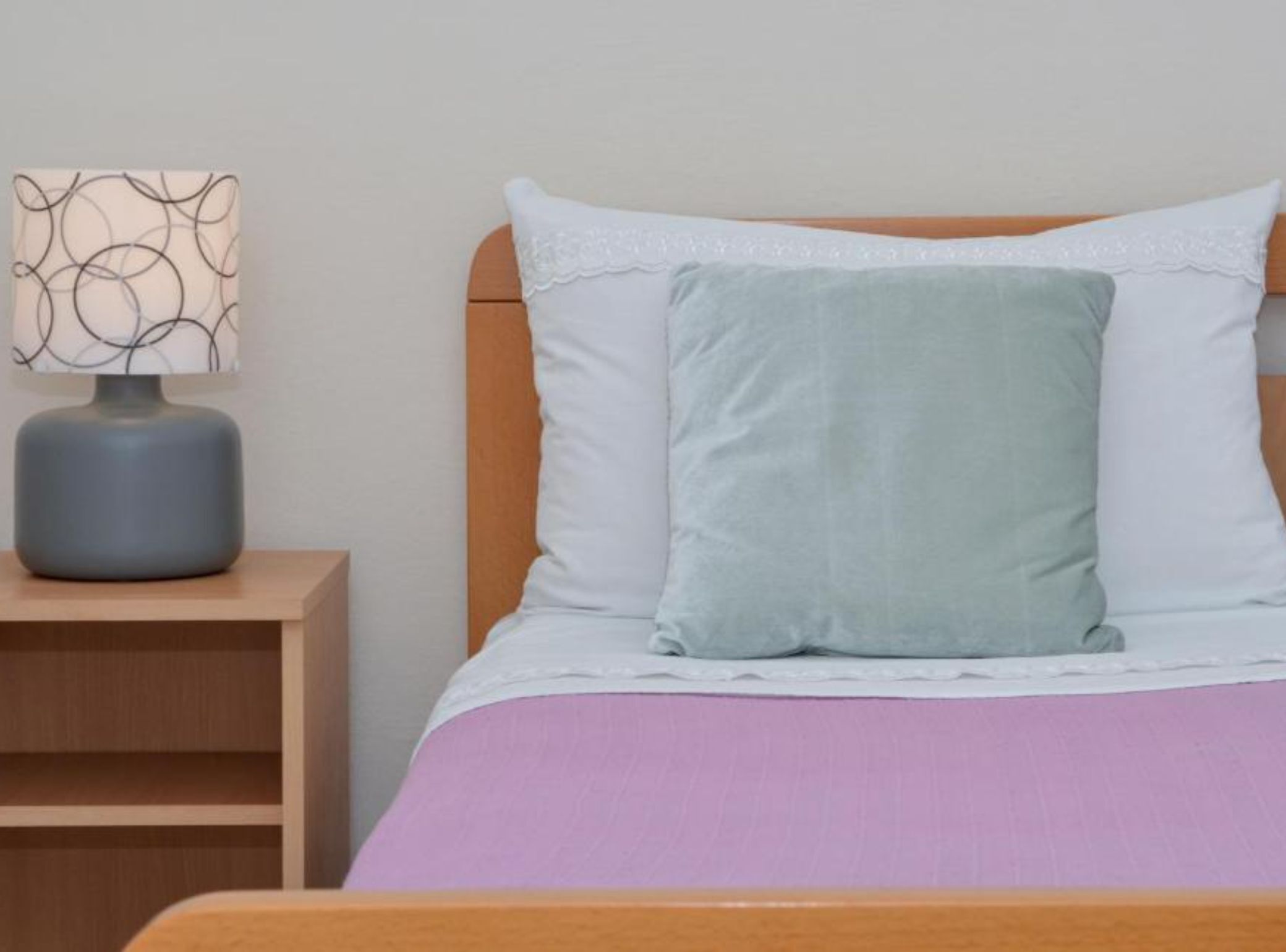 Un lit avec une tête de lit en bois, une table de chevet avec une lampe et une couvre-lit violette.
