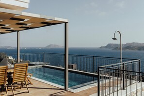 A pool area with a view of the sea, a pergola, and a table with chairs.